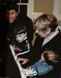 A woman and two boys playing piano together.