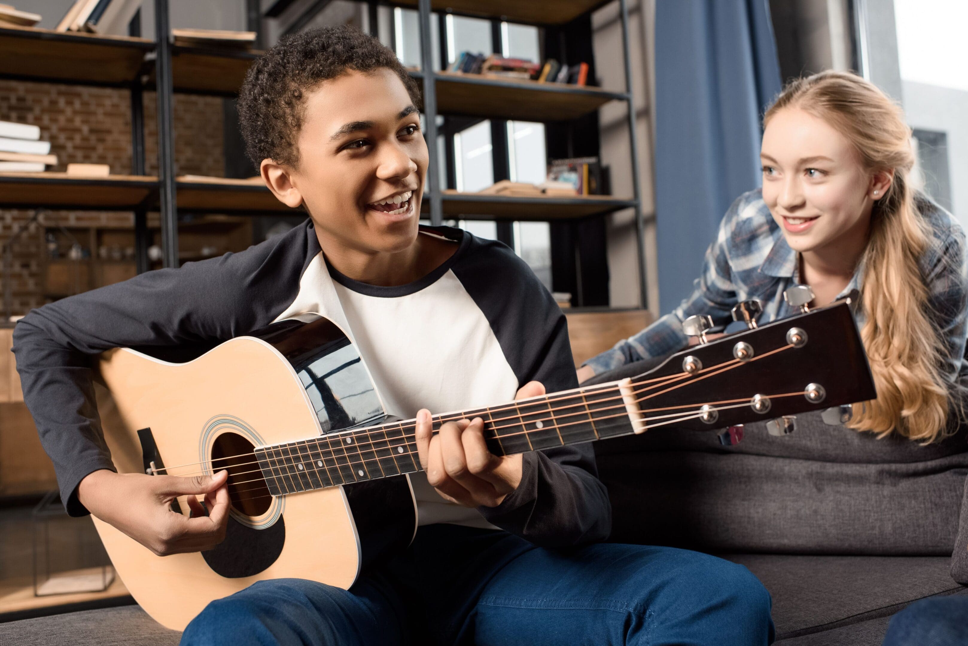 A man and woman sitting on the couch playing guitar.