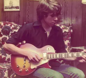 A man sitting on the couch playing an electric guitar.