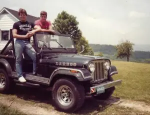 Two men sitting on the hood of a jeep.